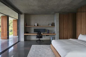A minimalist bedroom with concrete floors, walls, and furniture, featuring a large bed, a floating desk, and a built-in shelf