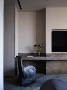 A minimalist living room with a concrete fireplace, wooden floor, and a single vase with purple flowers on a marble counter.