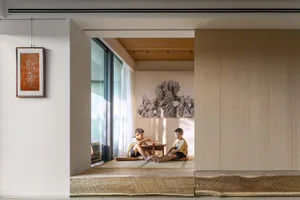 Two children sitting on a tatami mat playing a game in a minimalist living room with wooden paneling.