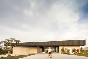 一座現代極簡住宅建築，外牆採用清水混凝土，在多雲的天空下呈現。