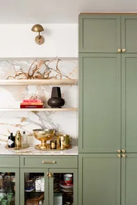 A modern green kitchen with marble countertops and brass accents.