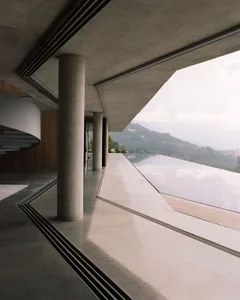 Modern interior with concrete and glass walls, featuring an infinity pool and a view of distant mountains.