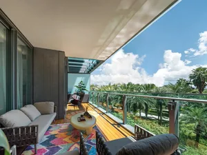 Modern outdoor balcony featuring a comfortable seating area with a colorful rug, a round table, and a scenic palm tree view.