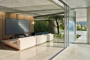 Contemporary living room with concrete walls and glass sliding doors overlooking a garden.