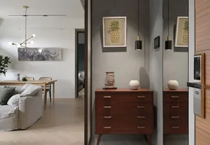 A modern minimalist living room with a grey sofa, wooden chest of drawers, and pineapple artwork on the wall.