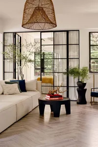 A modern minimalist living room features white furniture, a black coffee table with books, and potted plants with a wooden fl