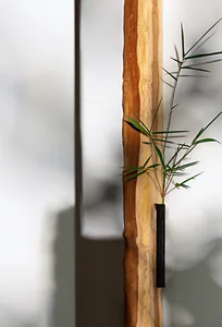 A modern decorative vase made of wood with a single sprig of greenery.