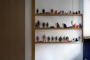 A wooden shelf with various toy figurines and dinosaur models arranged neatly on white walls.