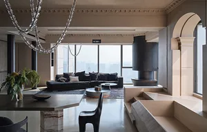 A modern living room with concrete flooring, a black sofa, large windows, and a large black fireplace.