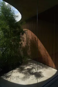 A minimalist interior design featuring a wooden wall with light shining through, casting shadows on a concrete floor.