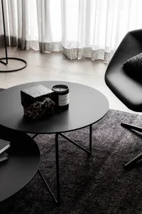 A modern, black metal side table with a candle, sculpture, and stack of books on it.