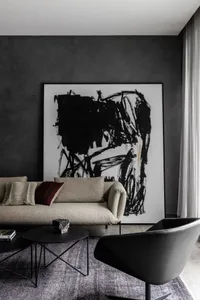 A modern living room featuring a beige sofa with decorative pillows, black tables, and a large black and white abstract paint