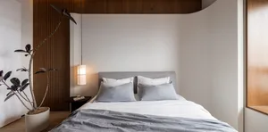Minimalist bedroom with a bed made from reclaimed wood, grey bedding, and a hanging lamp.