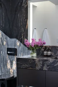An industrial bathroom with black marble walls and a black marble countertop, featuring purple flowers in a vase and a black 