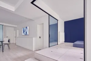 Modern minimalist living space with white walls and wooden floor, featuring a sliding glass door and blue storage compartment