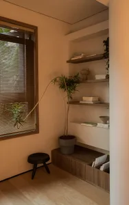 A minimalist interior featuring wooden shelves and a small stool near a window with closed blinds.