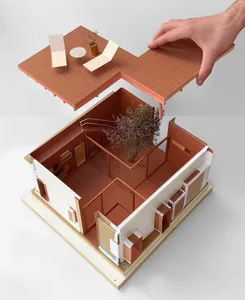 A model of a house made from paper and cardboard, with a tree inside and a hand lifting a section of the building.