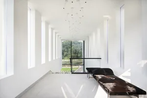 Minimalist interior with white walls and large windows featuring concrete and glass elements.