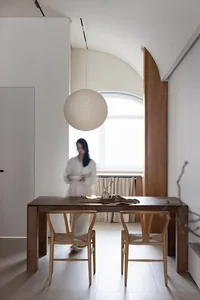 A modern living room featuring a wooden table, chairs, and pendant light, with a minimalist design and natural wood elements.