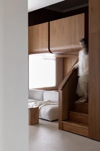 A modern living room with a large window, white sofas, and wooden cabinets.
