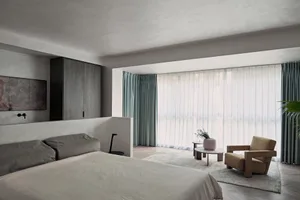Minimalist bedroom with textured finishes, large window, and comfortable seating area.