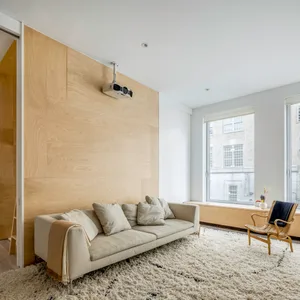 A modern minimalist living room with a wood accent wall, a white sofa, and a projector mounted on the ceiling.