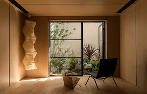 A modern minimalist lounge with a wooden floor, metal chair, and window with plants.