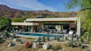 A modern residential architecture featuring a concrete, glass, and rock garden pool surrounded by cacti, flowers, and large b