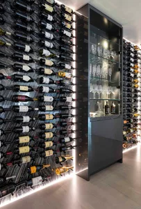 A modern wine cellar with bottles of wine stored on a marble wall and a glass cabinet displaying wine glasses.