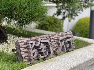A textured rock sculpture made of concrete with carved Chinese characters on a concrete ledge surrounded by greenery and gras