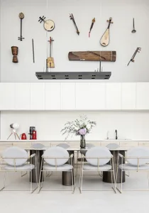A modern kitchen featuring minimalist design with metal dining table and chairs, white cabinetry, and musical instruments on 