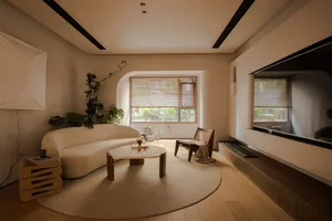 A minimalist living space featuring a beige suede couch, a round wooden coffee table, and a large window with natural light s