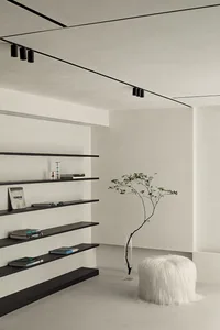 A minimalist living space featuring a concrete floor, floating shelves, and a white fur pouf with a potted plant.
