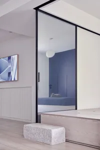 Minimalist modern bedroom featuring glass walls, a white round pendant light, and light wooden flooring with a single white b
