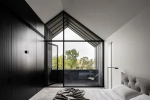 A modern bedroom with a black wall, a large window with a view of trees, and a bed with a textured headboard and blanket.