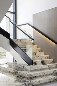 Modern marble staircase with black railings and a glass balustrade.