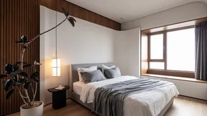 A minimalist bedroom with a bed dressed in white and gray linens, a wooden headboard, and a hanging white lantern-style light