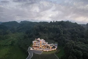 A modernist house with glass and concrete exteriors surrounded by lush greenery and mountains in the background.