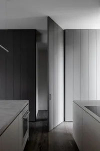 A modern minimalist kitchen with white marble countertops and dark wooden flooring.