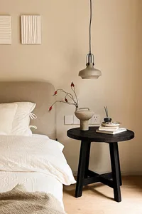 Minimalist bedroom featuring a black side table with a concrete vase, books, and incense sticks, alongside a white bed with s