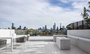 Modern outdoor terrace featuring grey concrete seating and a glass railing overlooking a city skyline.