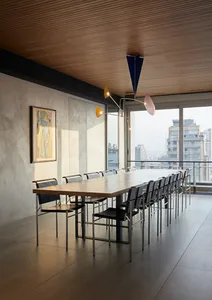 Modern office space featuring a long wooden table surrounded by black chairs, with a contemporary chandelier overhead and a l