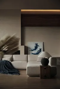 A modern living room with a beige sectional sofa, a dark lamp on a wooden side table, and a painting of silhouetted figures.