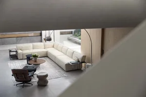A modern minimalist living room featuring a white sectional sofa, black lounge chairs, and a concrete floor.
