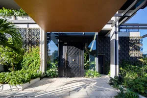 A modern entrance featuring glass and metal materials, with greenery and a geometric pattern on the walls.