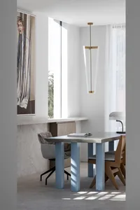 A minimalist home office featuring a metallic desk with blue accent columns, a sleek pendant light, and a large window with a