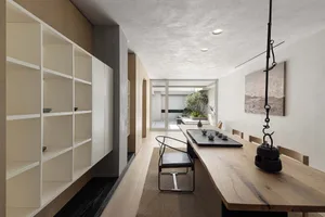 Modern minimalist living room with a wooden floor, white walls, and a long wooden table.