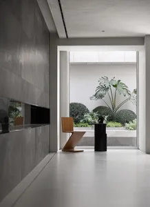A modern lobby interior with a concrete floor, minimalist furniture, and a view of a green courtyard.