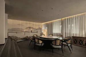 Modern dining room with concrete elements and a round dining table surrounded by black and gold chairs.
