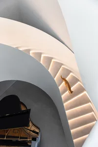 A modern staircase with concrete steps and a white railing illuminated by warm light.